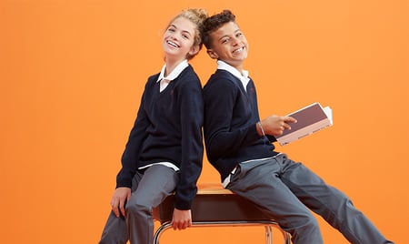 two smiling kids in uniform sitting on a desk 